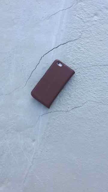 Brown phone case lying on cracked light blue wall surface.