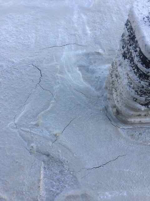 Close-up of a snow-covered roof with ice cracks and a metal pipe in the snow.