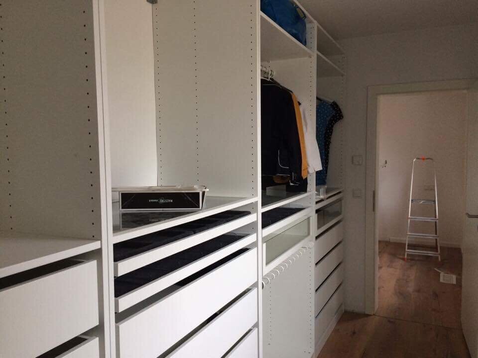 White walk-in closet with open shelves, drawers, and hanging rod, ladder in hallway