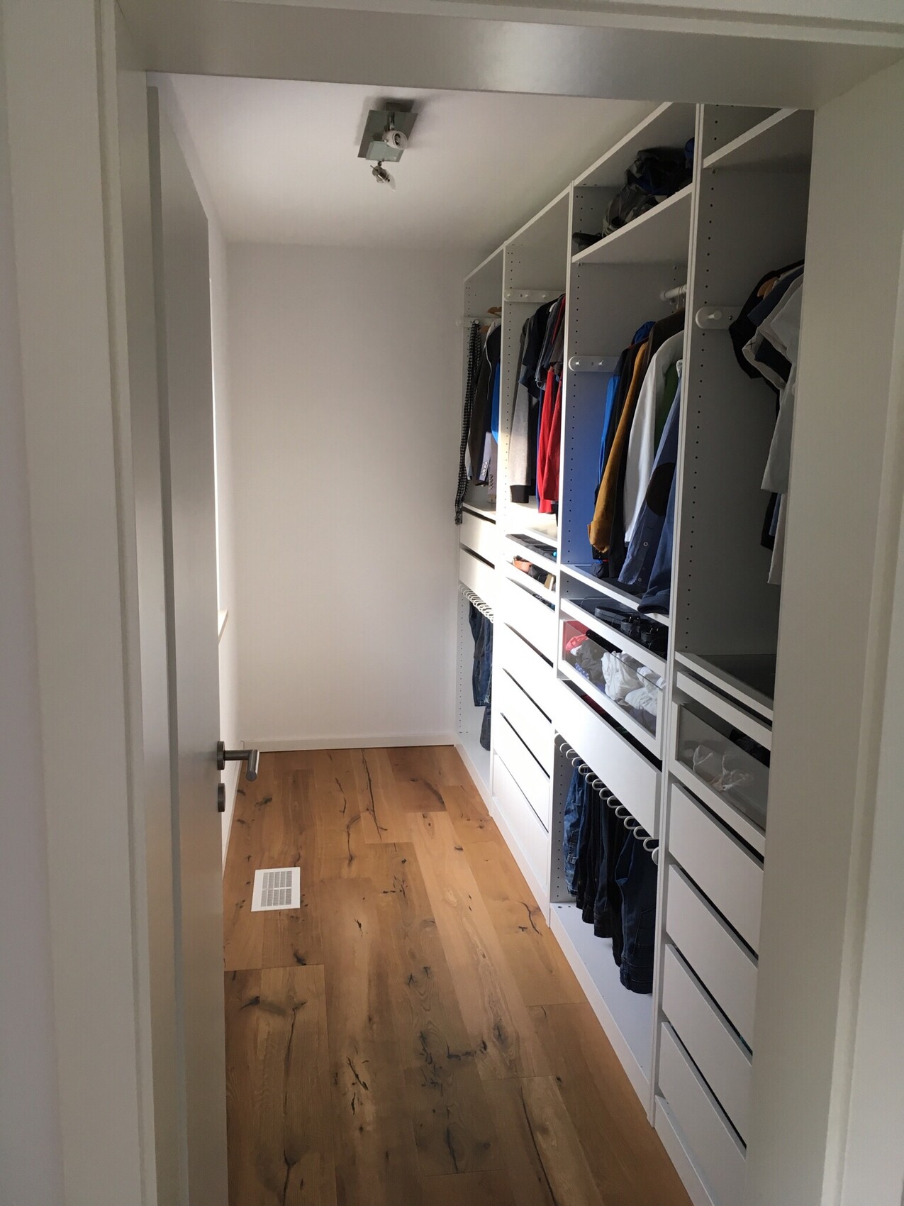 White walk-in wardrobe with shelves, hanging rods, and wooden floor