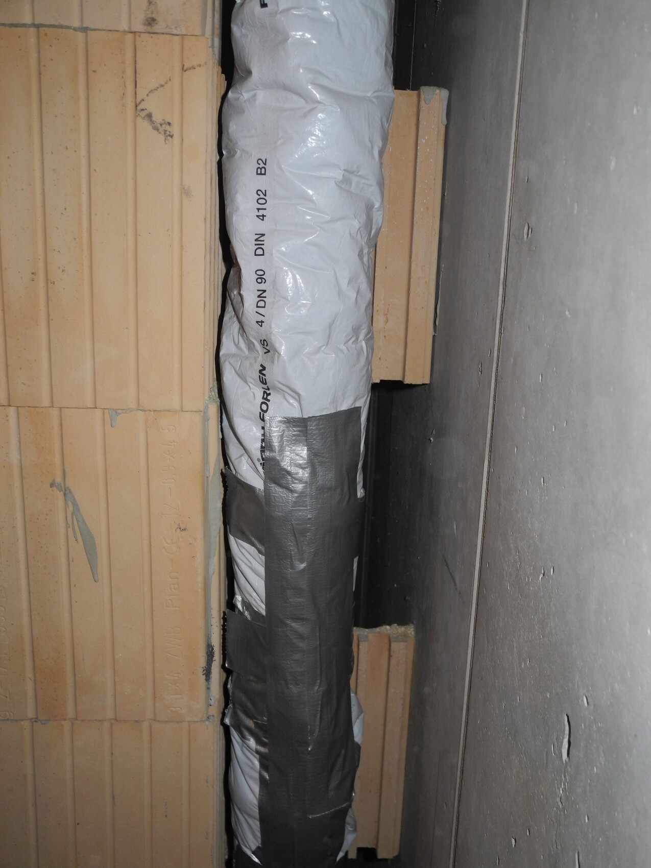 Insulated installation pipe in a construction wall between wooden battens and concrete wall.
