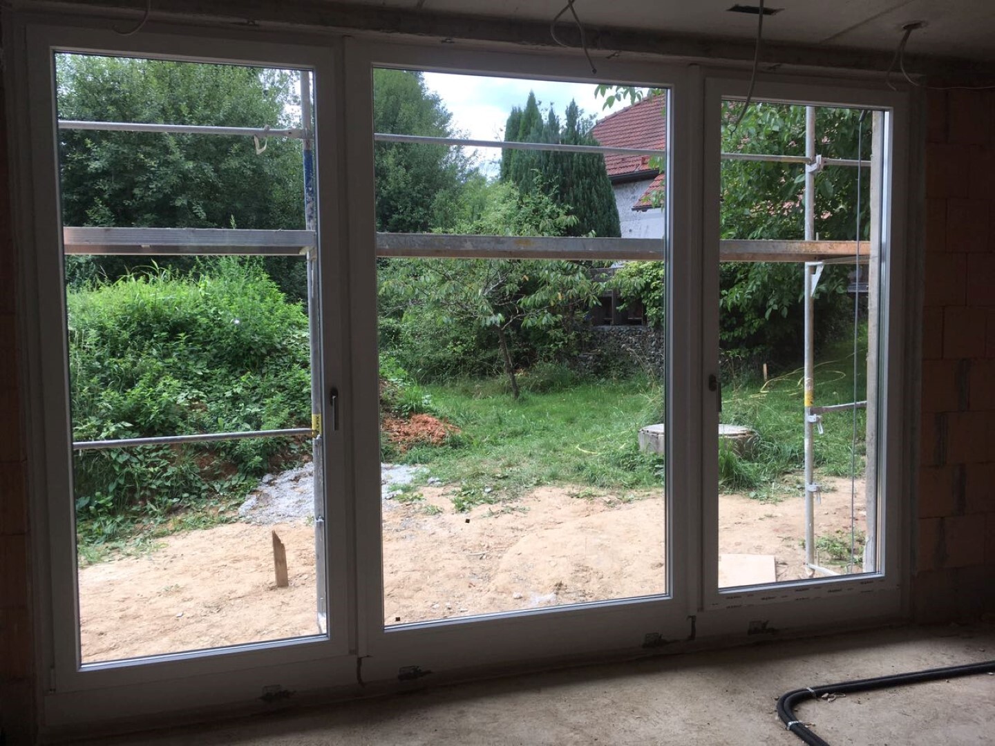 Large interior window during construction work, view to garden with scaffolding outside.