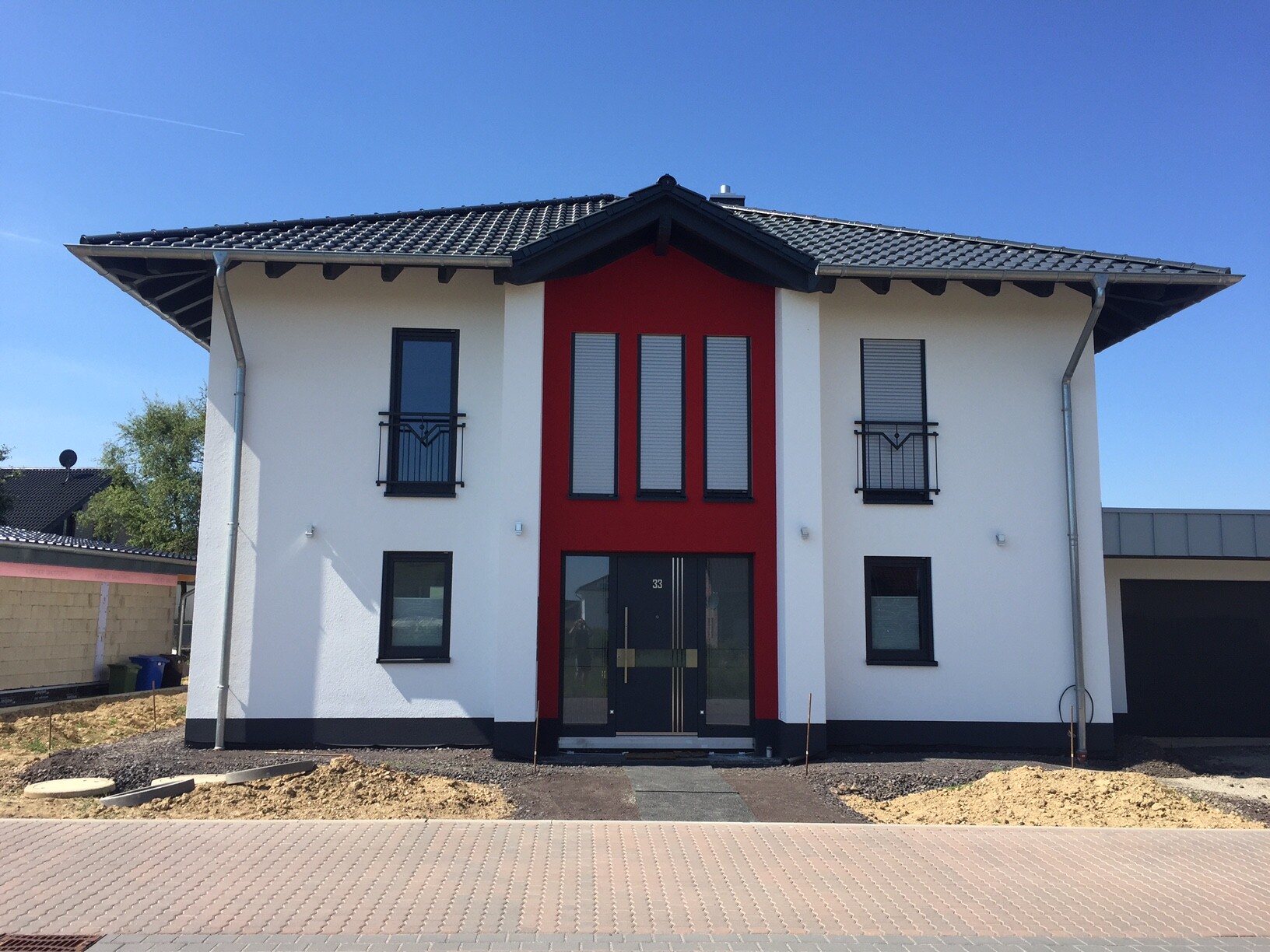 Modern two-story villa with a red central section, black windows, and garage.