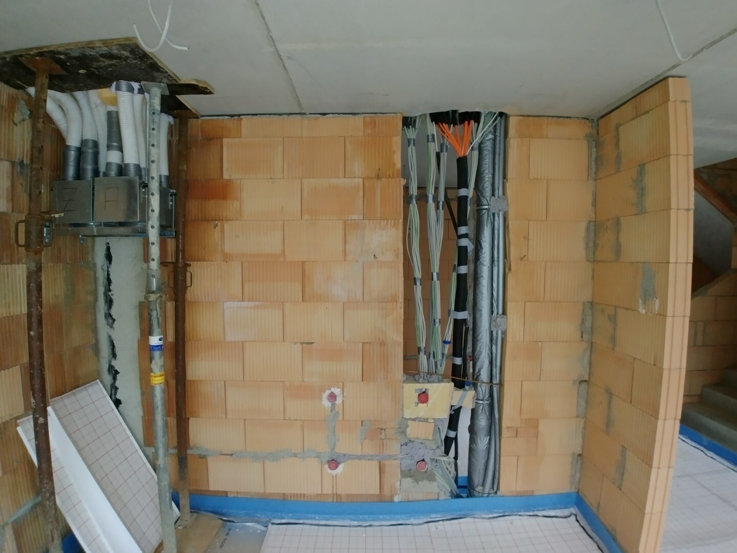 Interior of a construction site with brick walls, cable bundles, pipes, and installations.