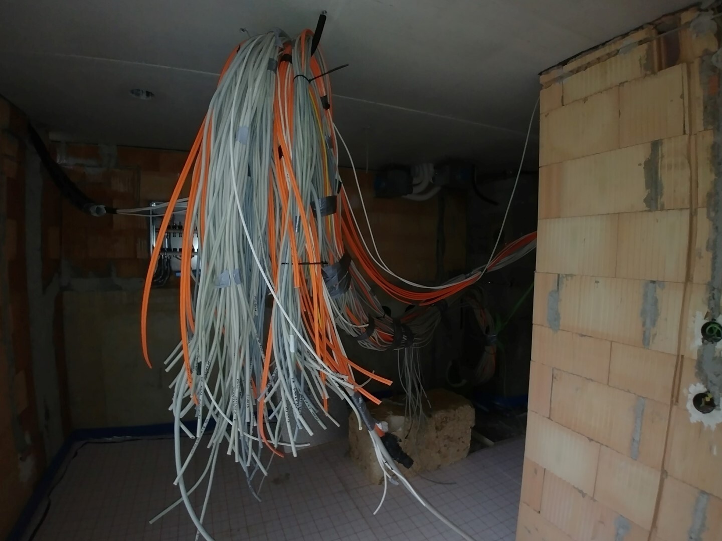 Numerous orange and white electrical cables hanging untidily from the ceiling of a shell construction.