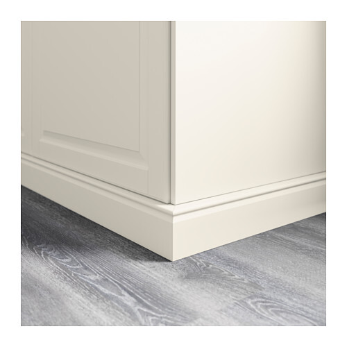 Close-up of the lower corner of a white cabinet with base on a gray wooden floor.