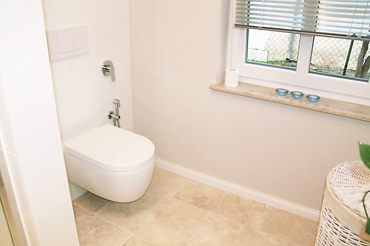 White modern bathroom with wall-mounted WC, windowsill with toilet paper and blue bowls.