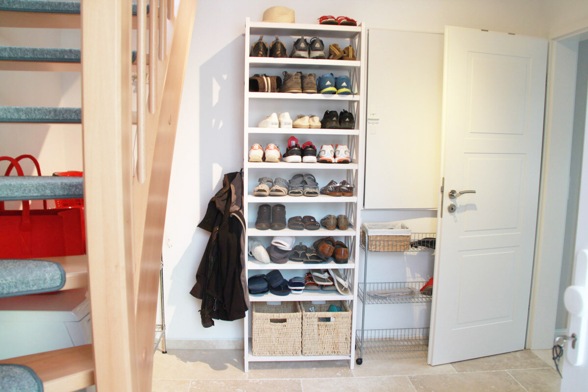 Entrance area with white shoe rack full of shoes next to the door and staircase.