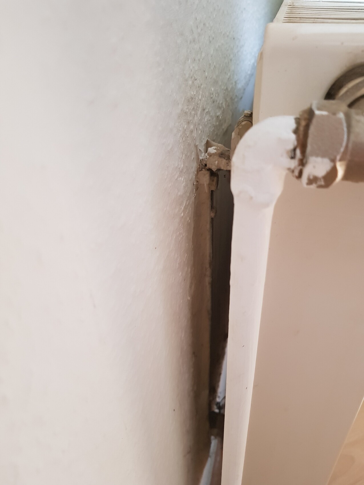 Close-up of a radiator with a crack and peeling plaster on the wall.