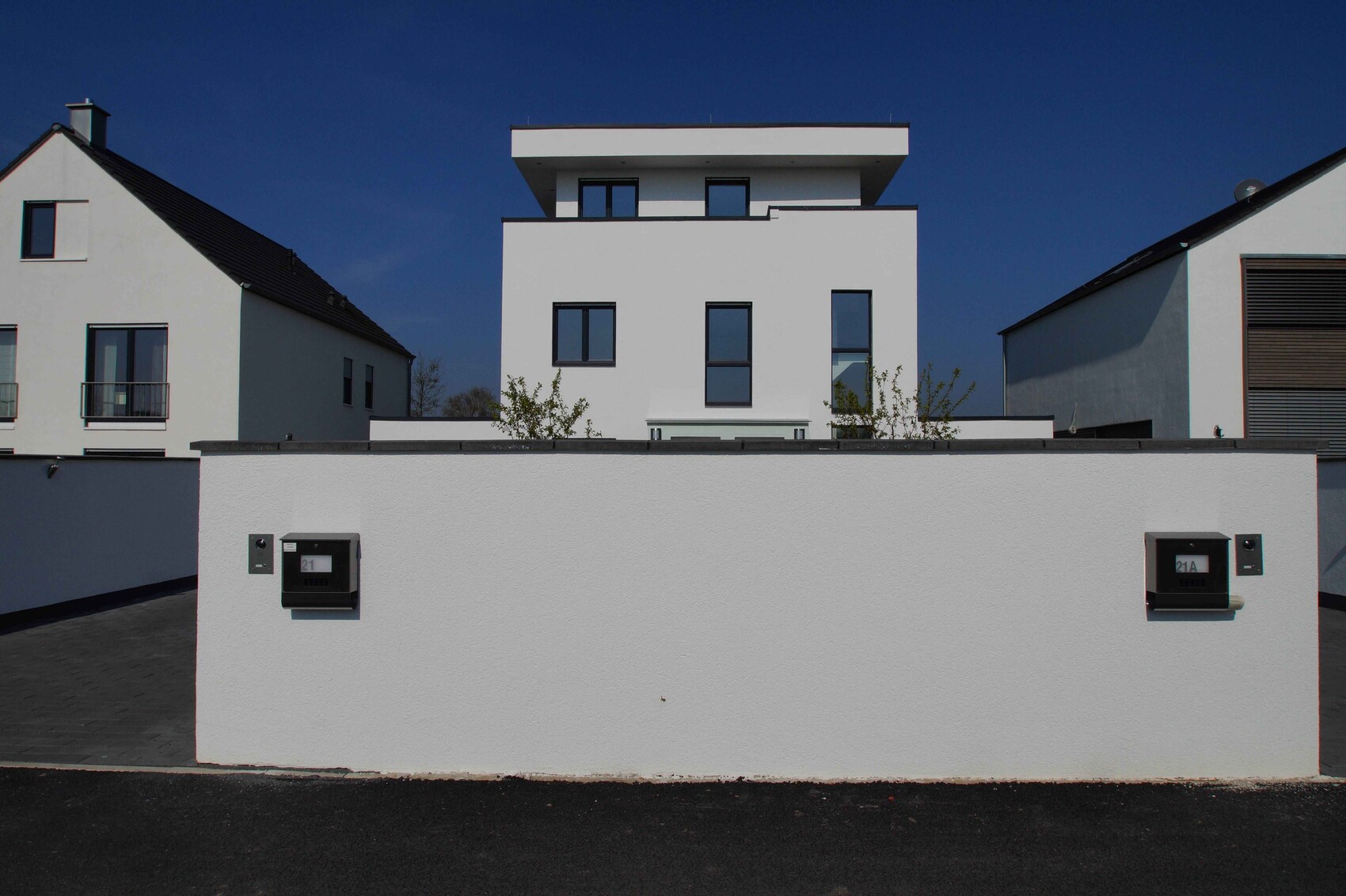 Modern white residential buildings behind a white wall; two mailboxes attached to the wall, blue sky.