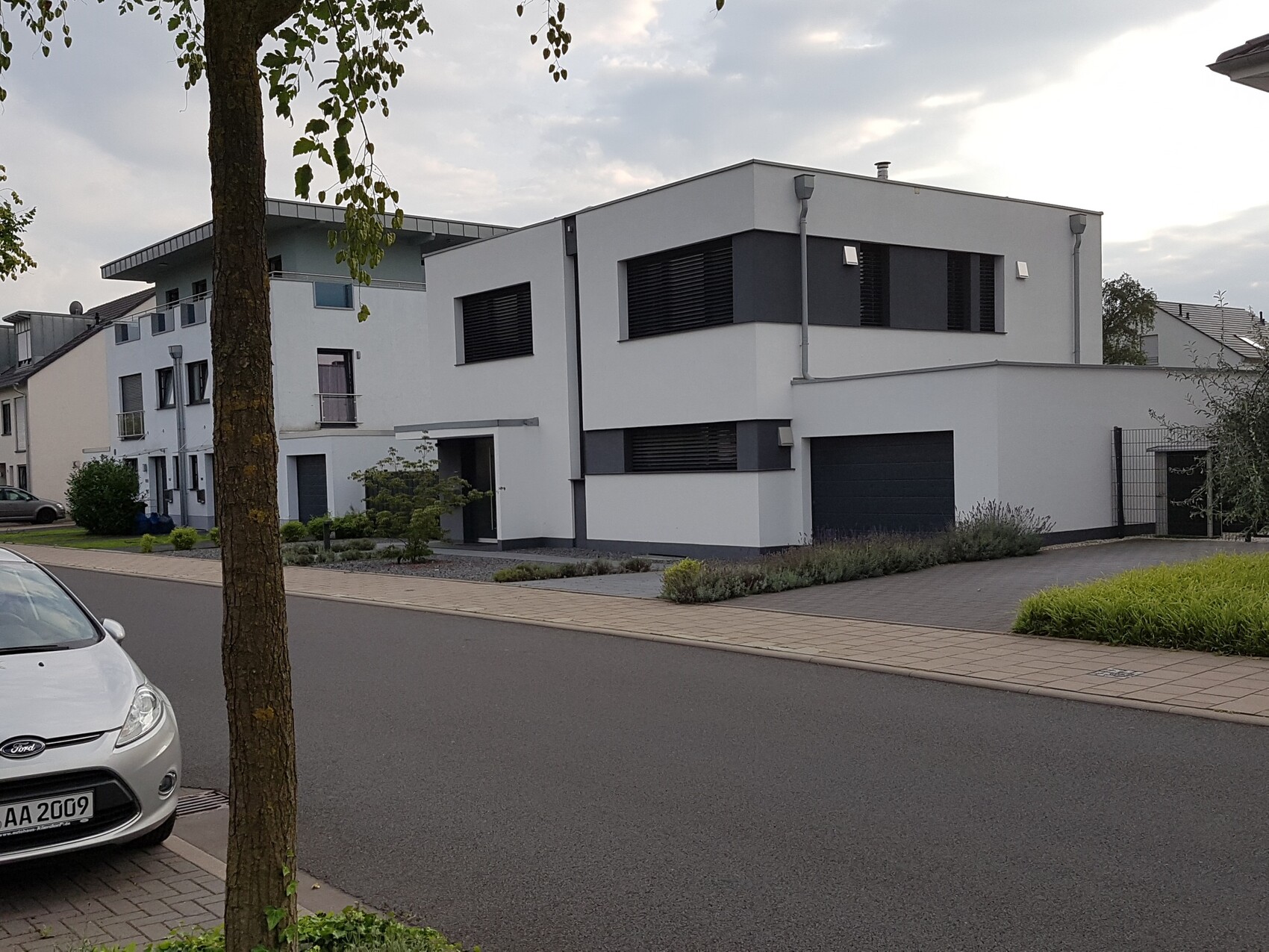 Modern housing development with white buildings, garage, sidewalk, and parked car at street side.