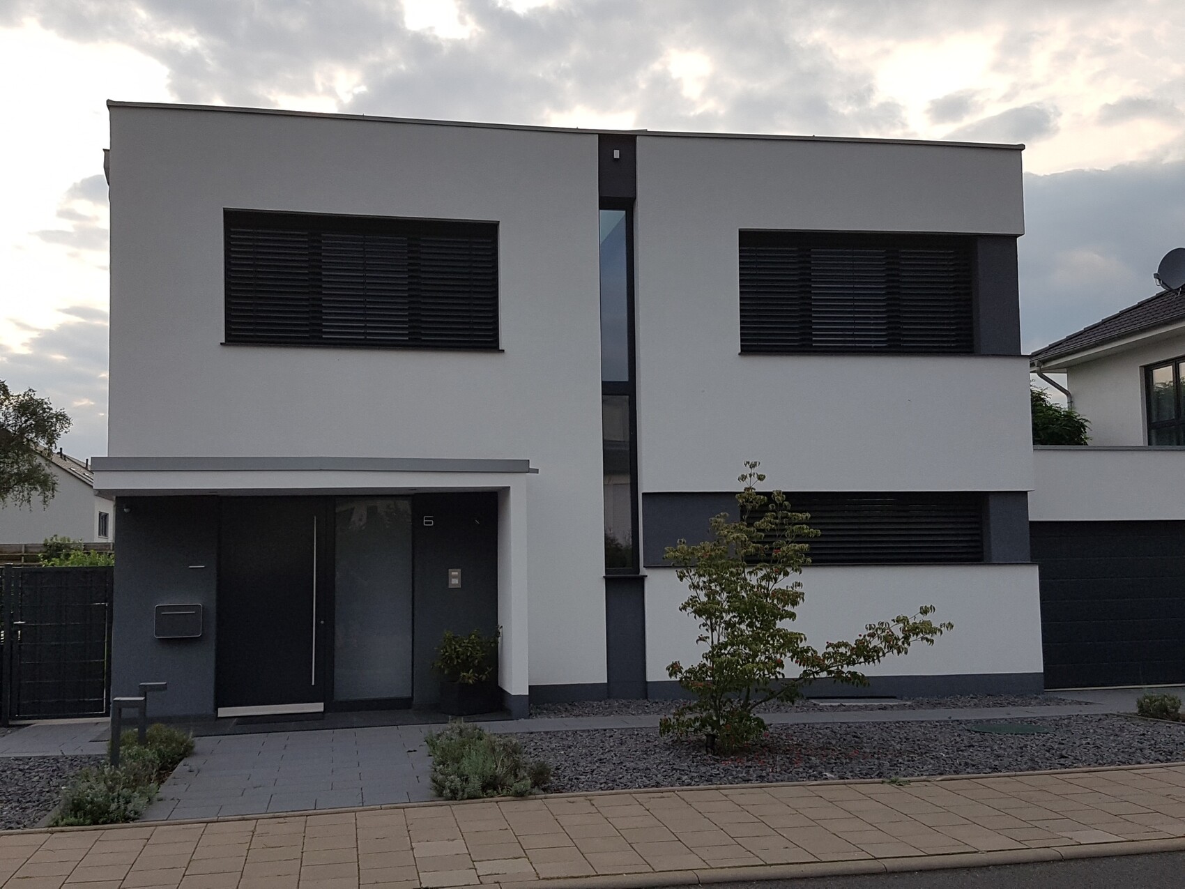 Modern two-story house with white facade, dark shutters, and gravel garden.