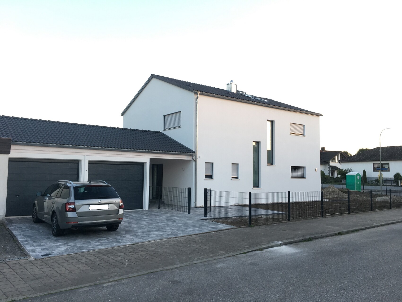 Modern white villa with garage; grey station wagon parked in front, fence around the property.