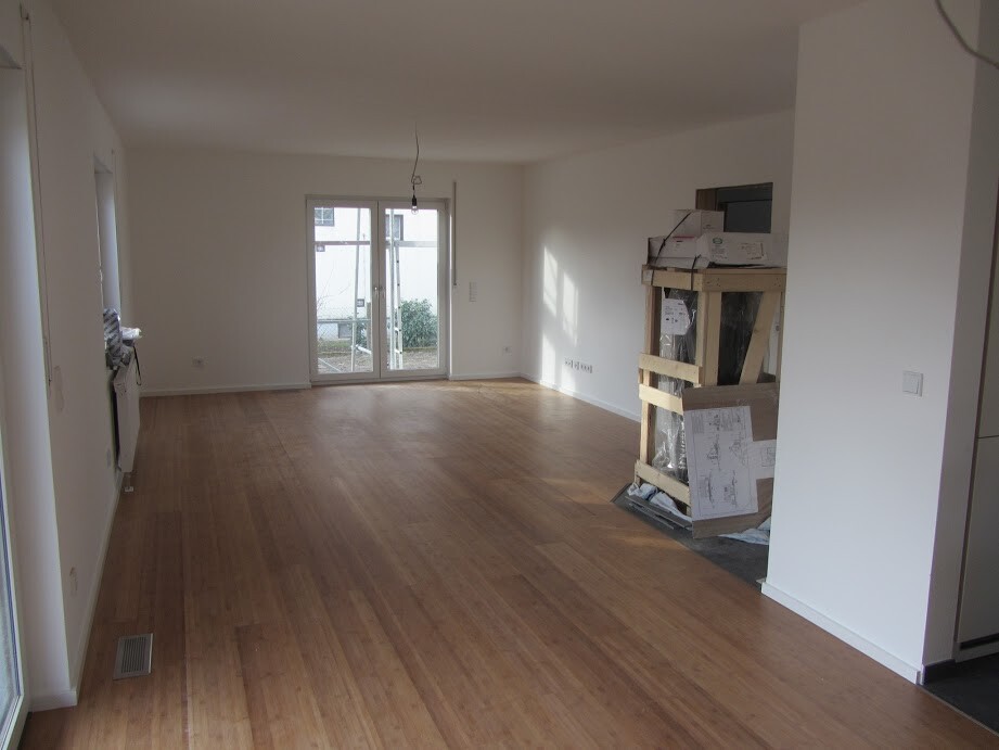Empty living room with wooden floor, glass door to outside, provisional wooden structure with boxes on the right.