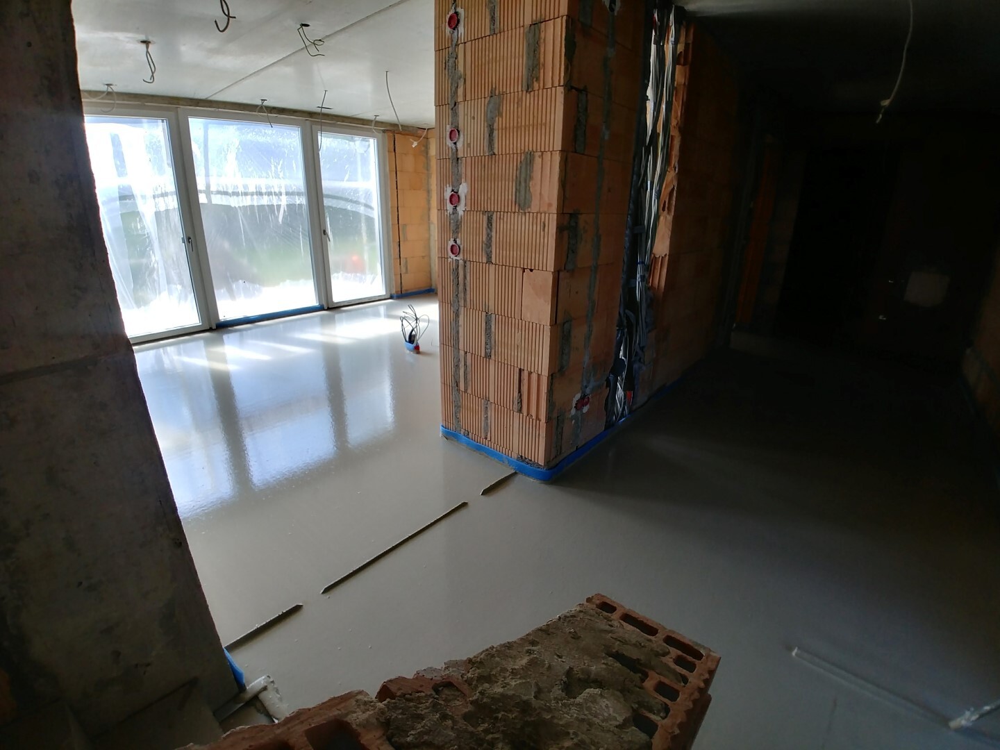 New-build interior: brick wall, installation pipes, smooth floor, large window façade.