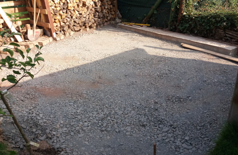 Construction site with gravel base, stacks of wood, and timber at the edge