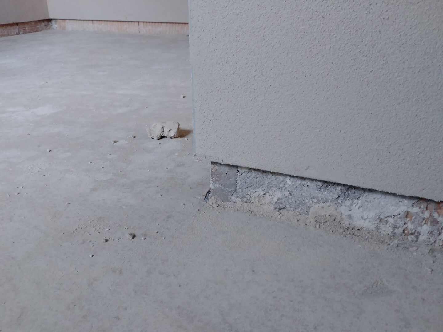 Unbearbeiteter Rohbau: Betonboden mit Fundamentabschluss am Wandfuß einer Hauswand.