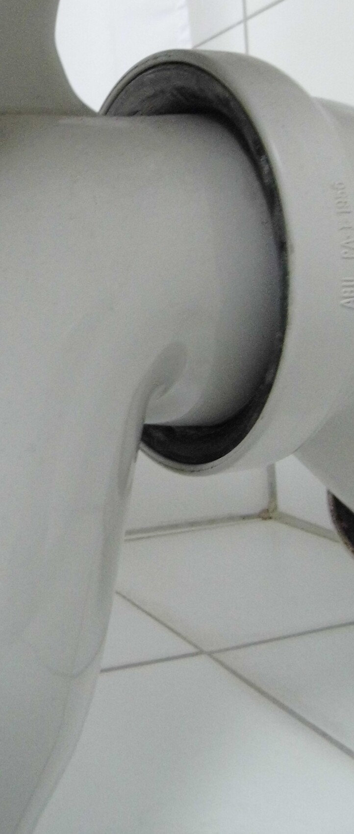 Close-up of a gray plastic joint with a round opening; tiled floor in the background.