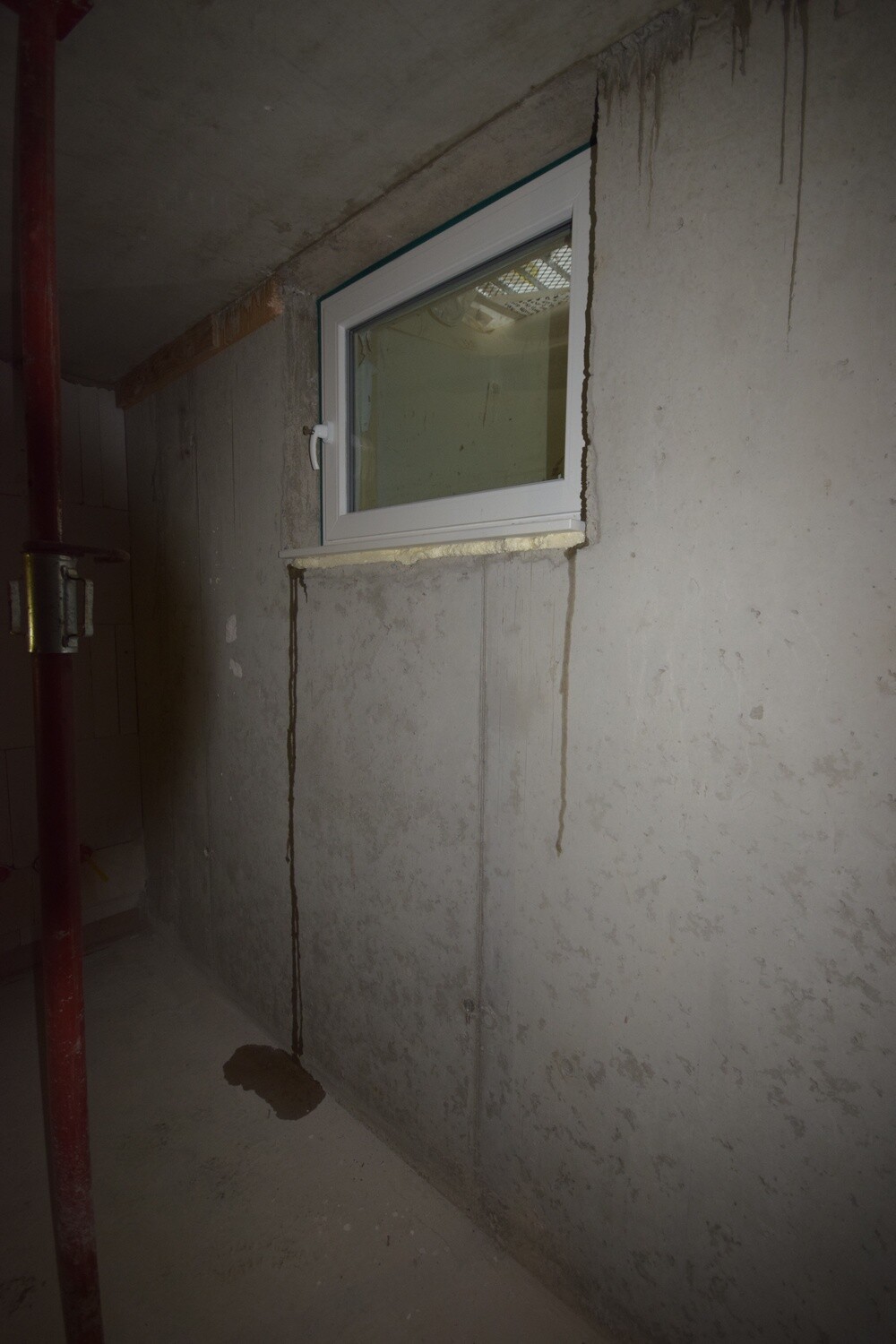 Kellerfenster in roher Betonwand während Bauphase, Feuchtigkeitsspuren sichtbar