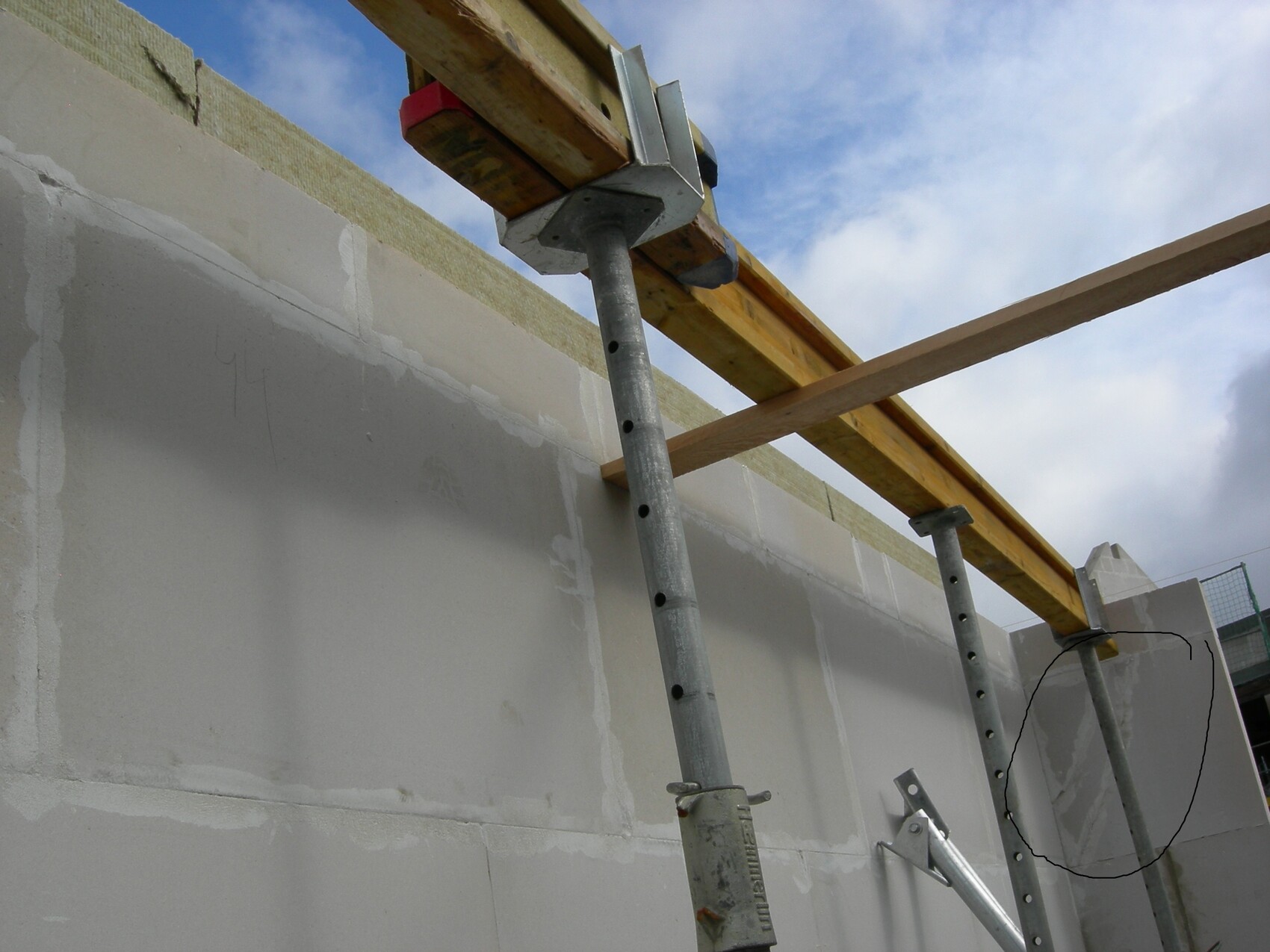 Construction site with concrete wall, wooden girders, and metal scaffolding under a blue sky.