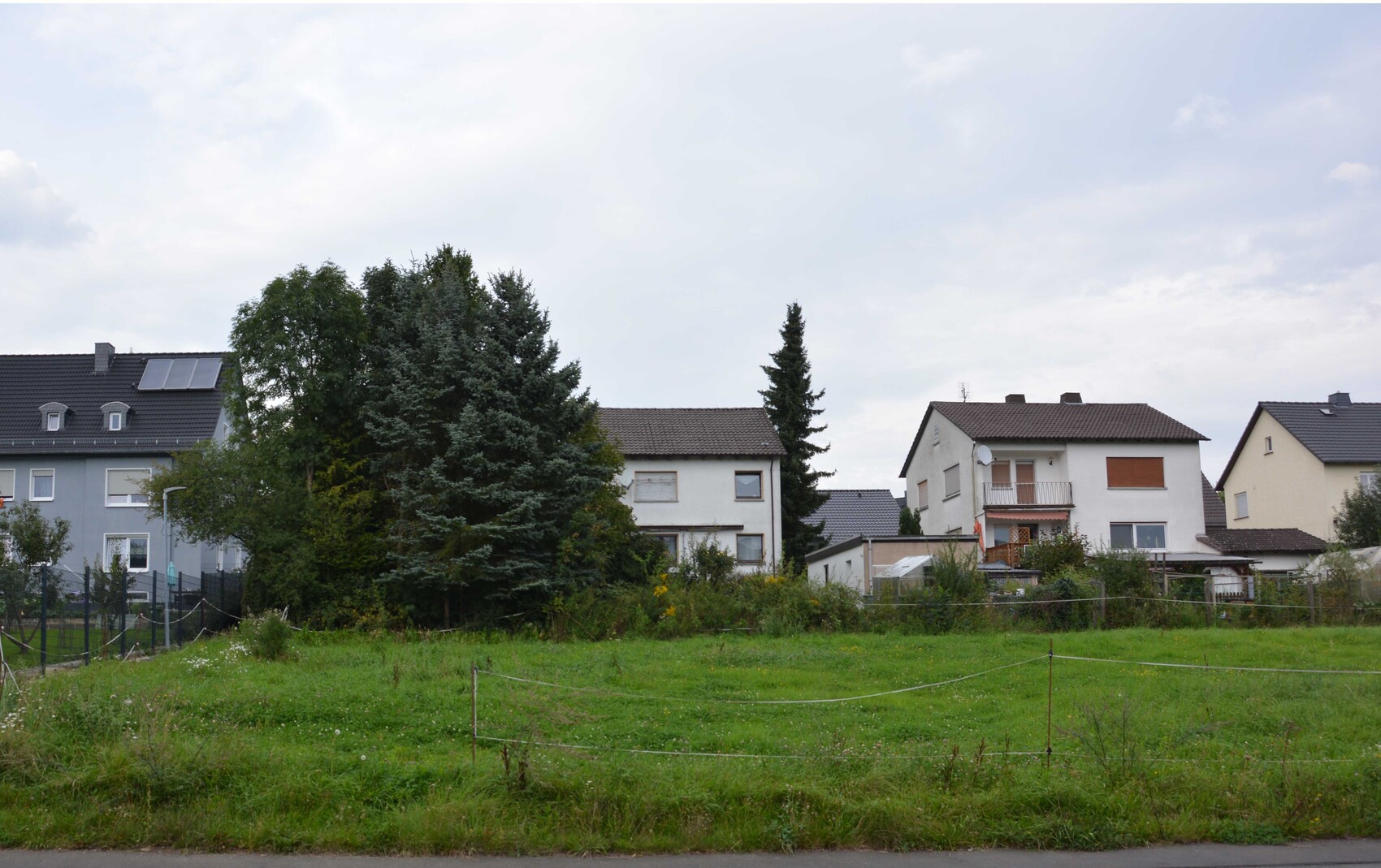 Green building plot with trees and adjacent houses in a residential area.