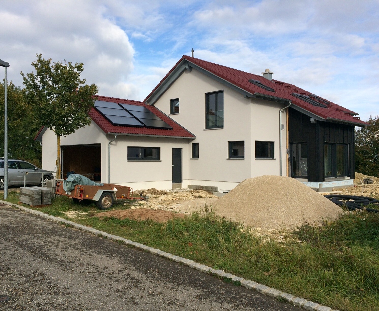 Under construction red gable roof, solar panels, tree on the left, gravel mound in the foreground.