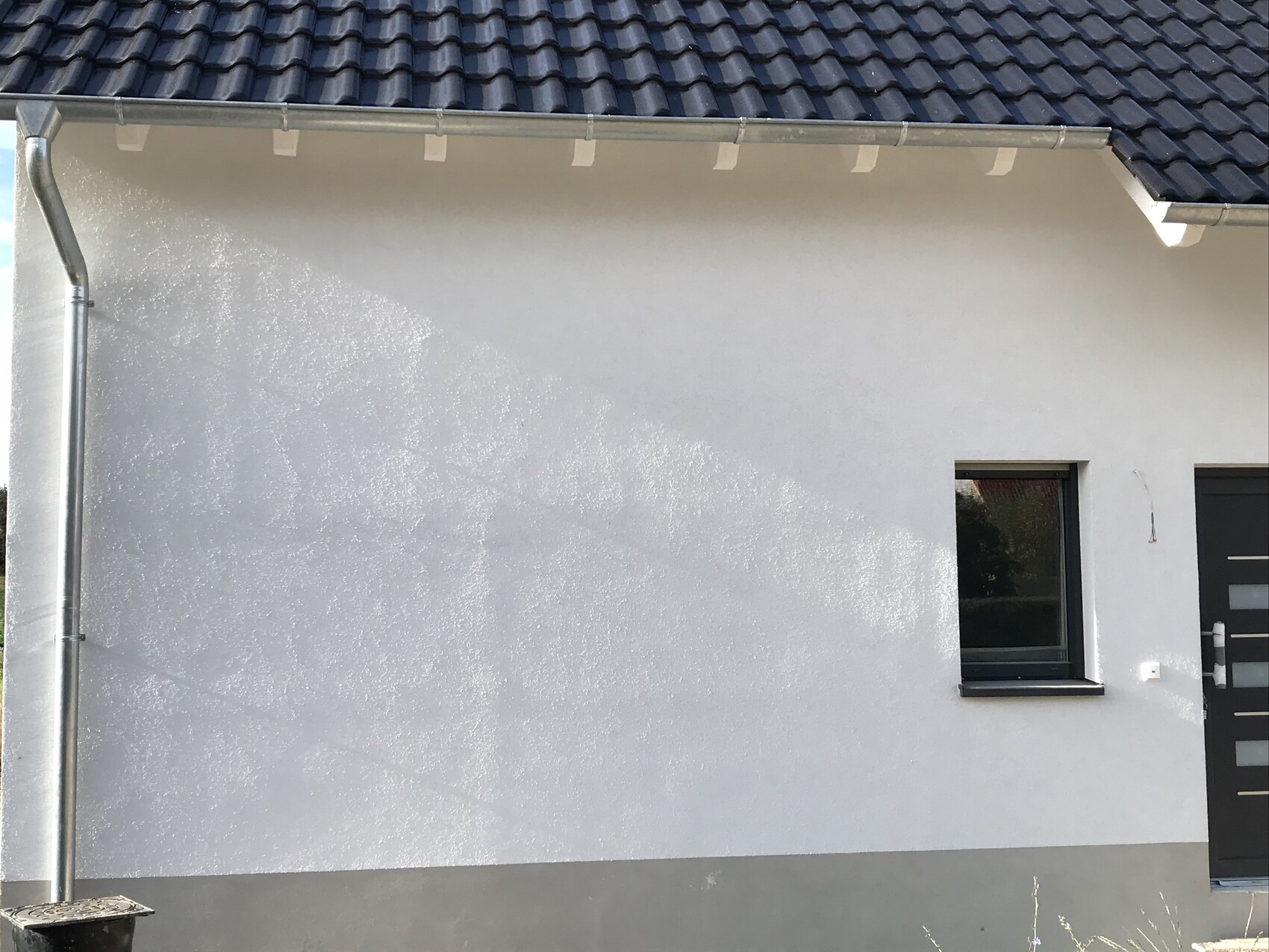 Exterior view of a house wall with window and door, gutter visible