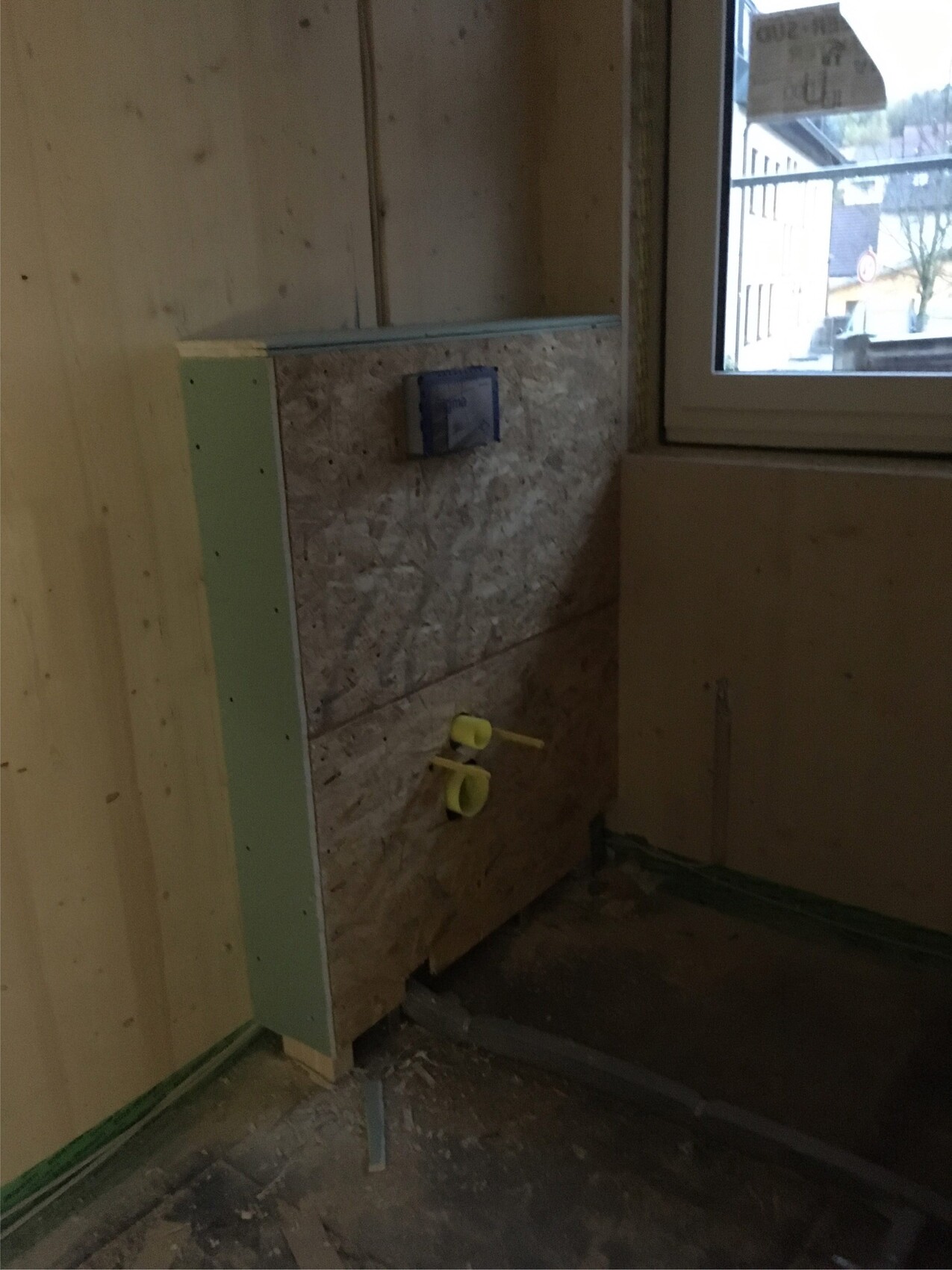 Badezimmer-Rohbau: OSB-Wandverkleidung, sichtbare Sanitärrohre und Bauarbeiten am Fenster