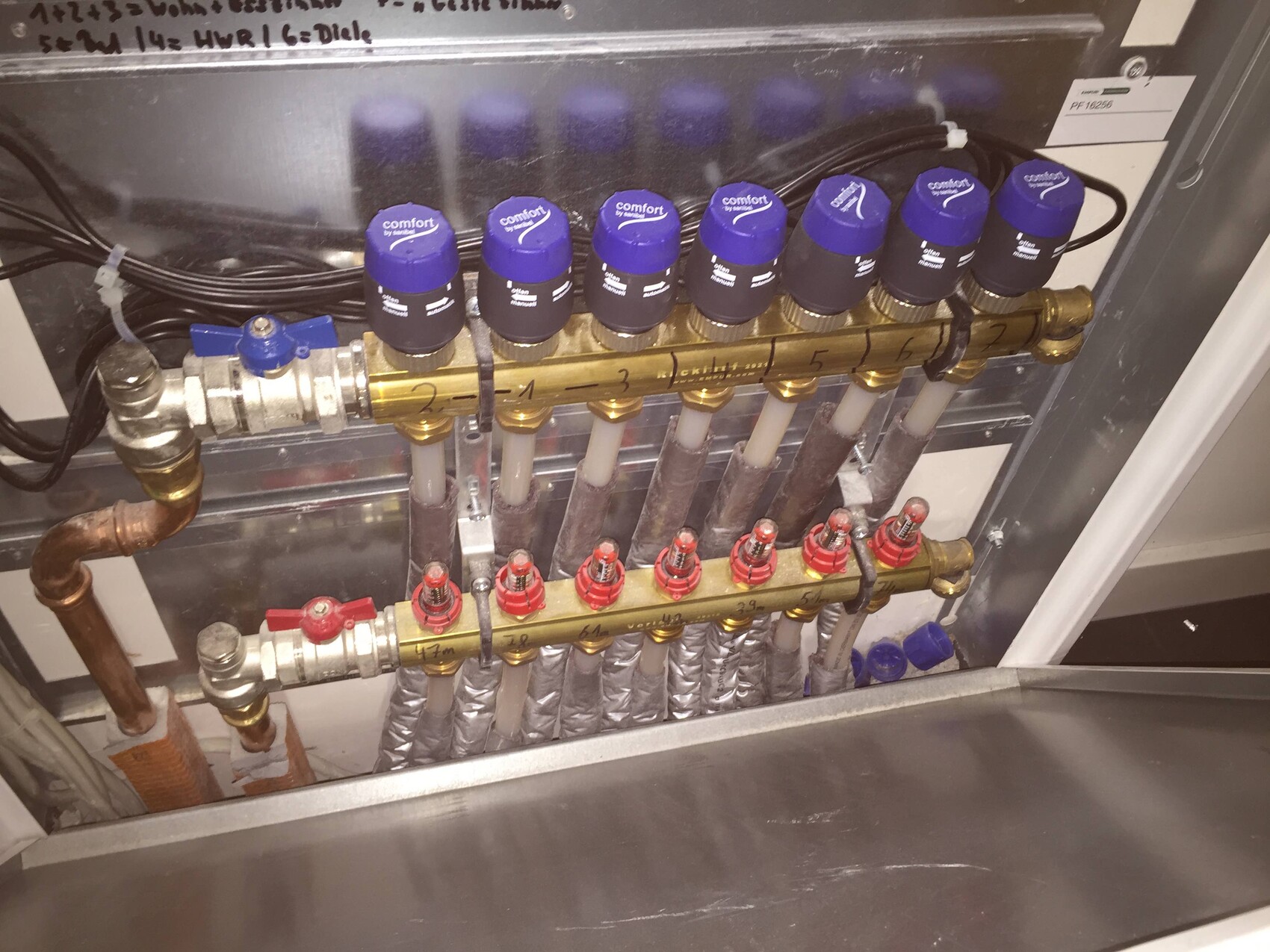 Manifold for heating circuits with six pipes, blue valves at the top, red shut-off valves at the bottom.