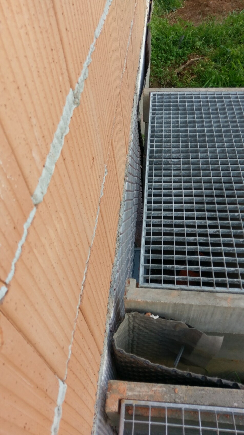 Außenwand aus orangefarbenen Backsteinen mit Fugen und Metallgitterrost am Boden