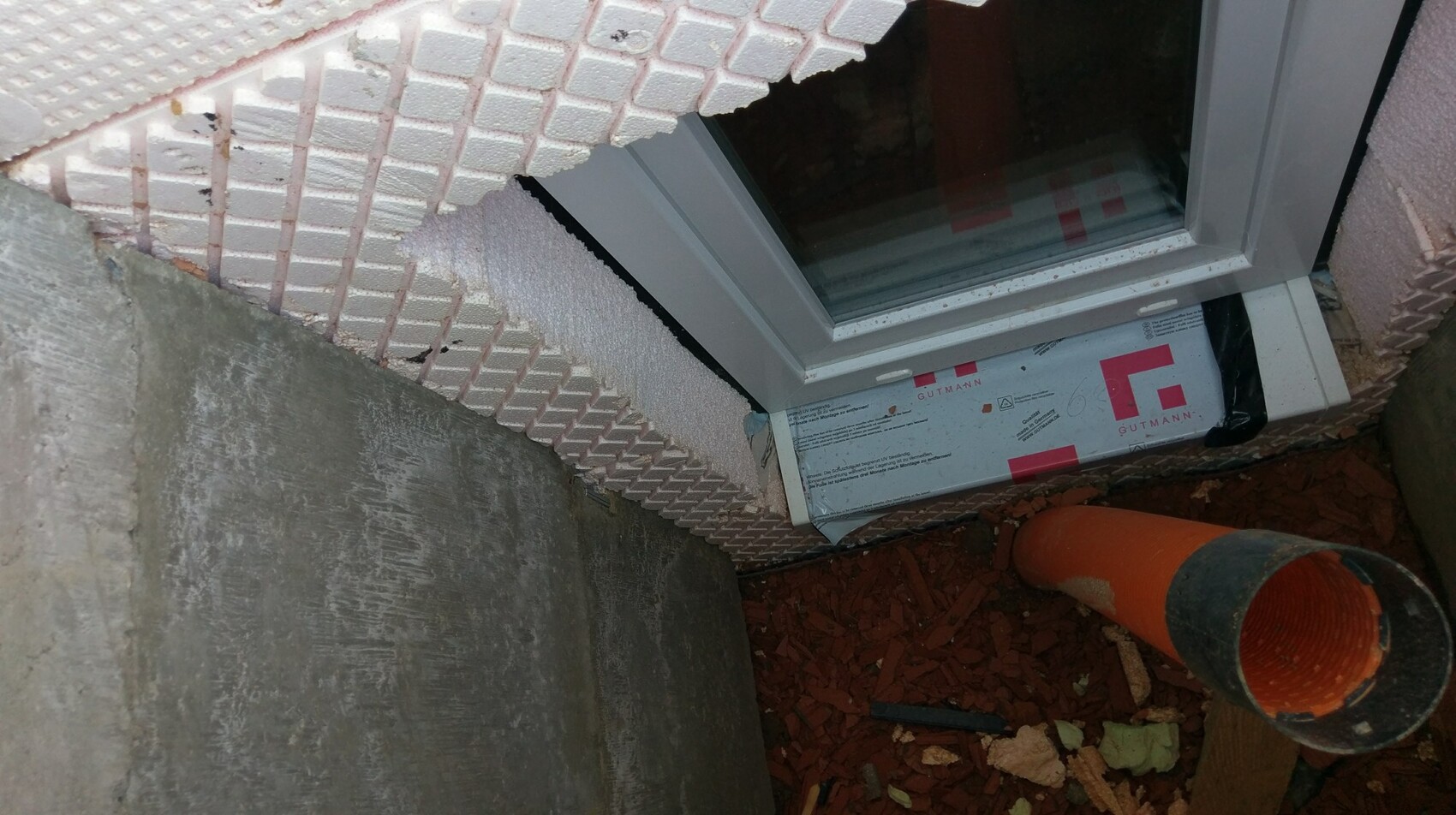 Fensterinstallation im Kellerbereich mit Dämmung und Rohr