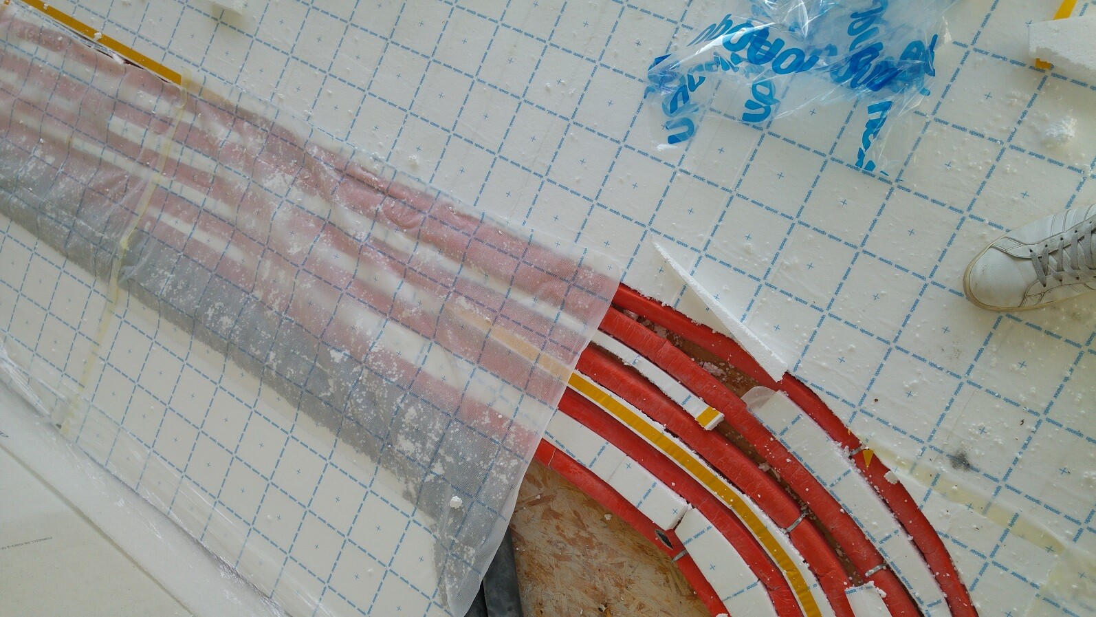 Rote Heizrohre werden im Bau installiert, umgeben von Dämmplatten und Folie.