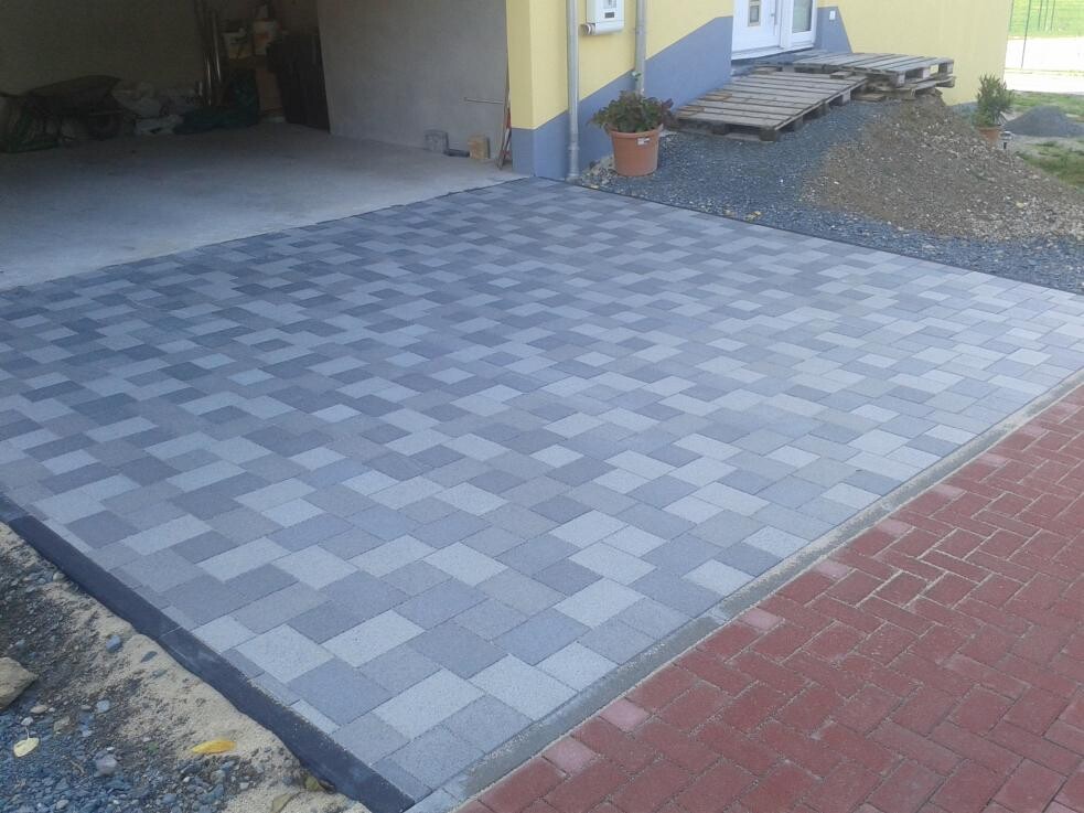 Paved driveway with gray squares in front of a yellow house with garage