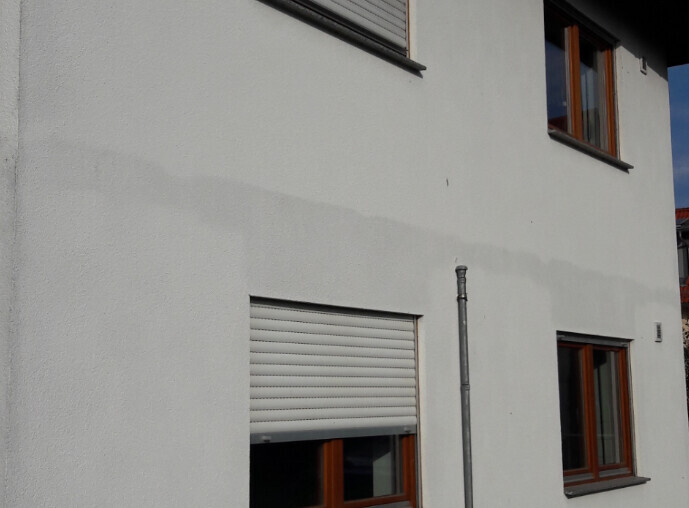 Exterior view of a house with white facade, wooden windows and roller shutters