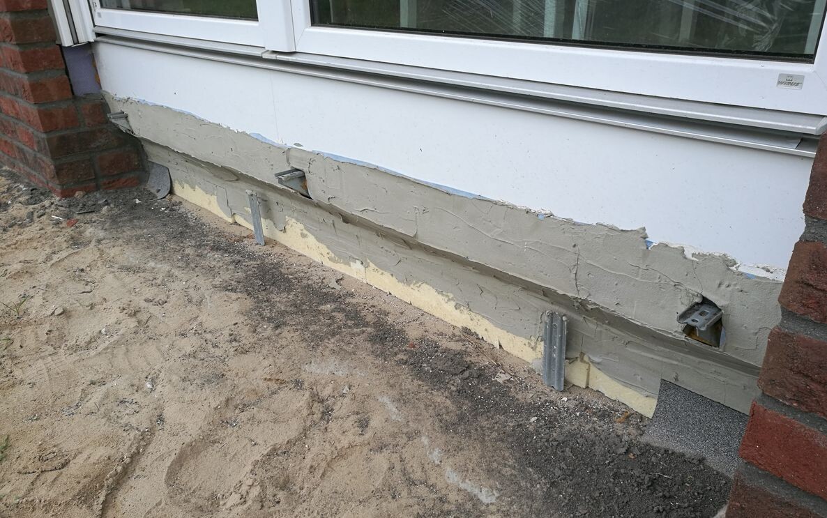 Exterior wall at the lower plaster area with cracks and visible insulation at the foundation