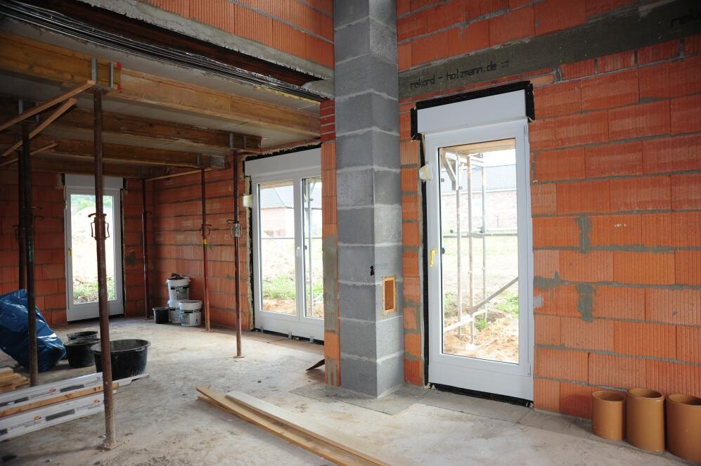 Interior of a construction site: red brick walls, concrete column, glass doors, construction timber and buckets