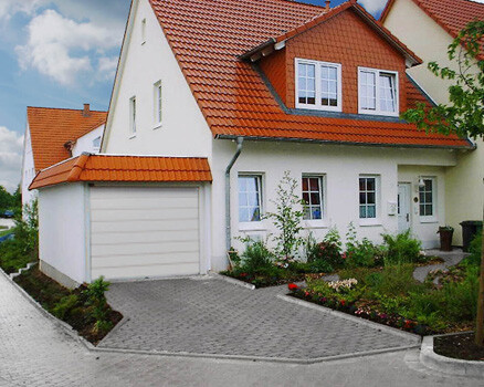 Exterior view of a white single-family house with a red roof and garage at the driveway.