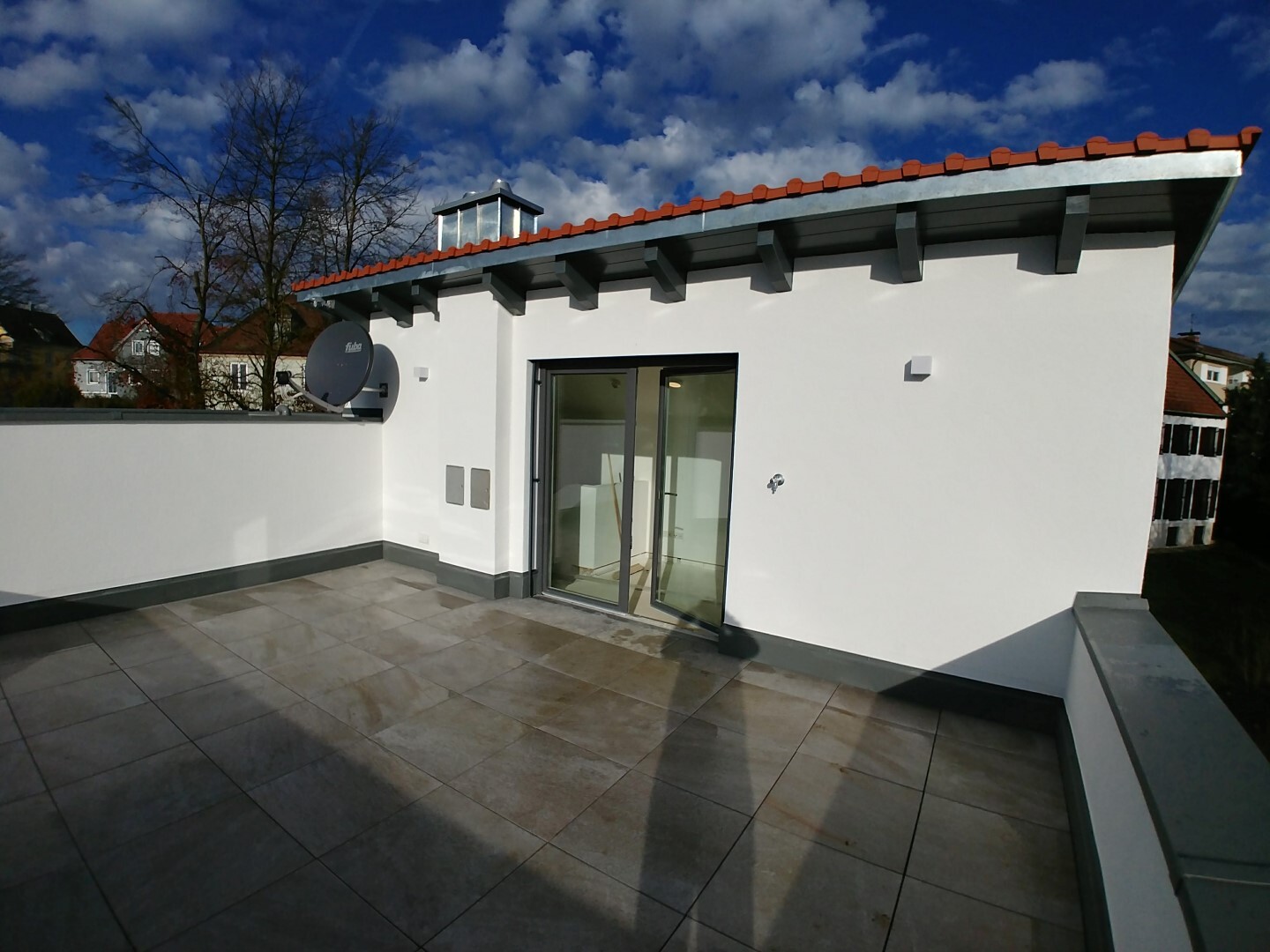 Roof terrace of a white modern building with glass sliding door and satellite dish.
