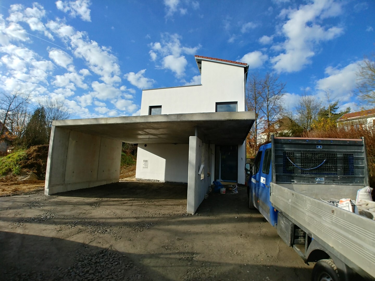 Modern white house structure with carport, construction truck beside it, blue sky.