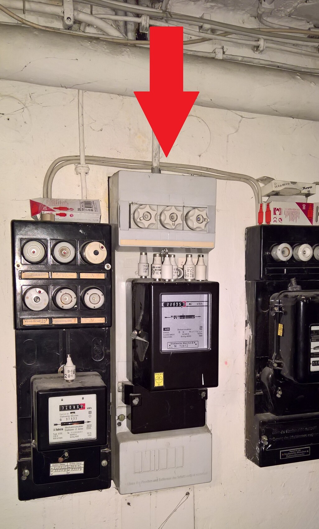 Large red arrow marks main distribution box next to other meter and fuse boxes on basement wall