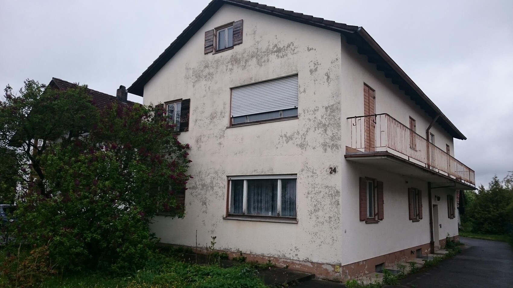 Exterior view of a two-story house with balcony and weathered facade.