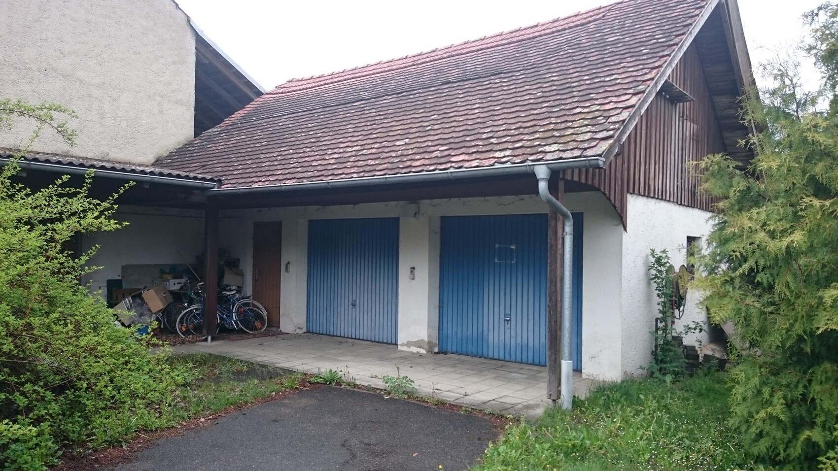 Exterior view of a building with two blue garage doors, bike storage area, and roof overhang.