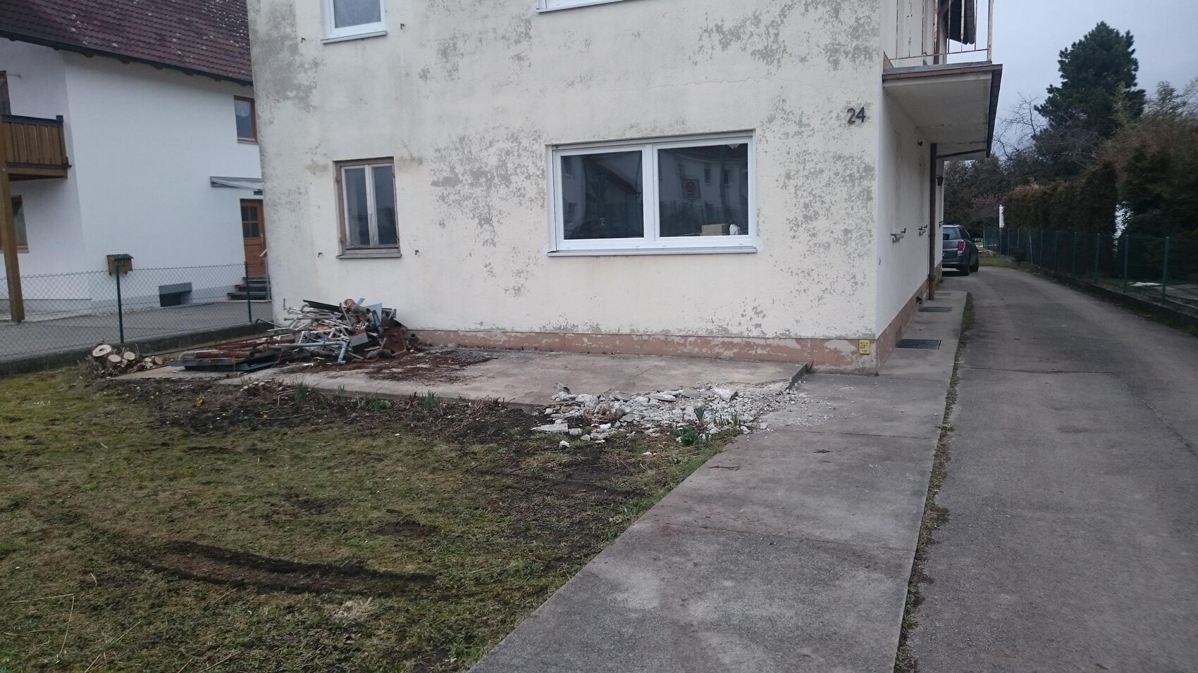 Exterior wall of a multi-family house with peeling plaster and construction debris in front.