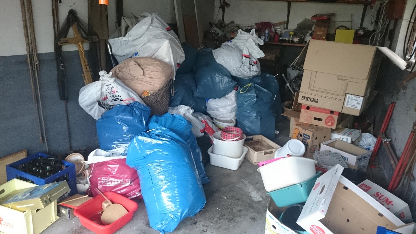 Untidy garage with many garbage bags, boxes, and tools.