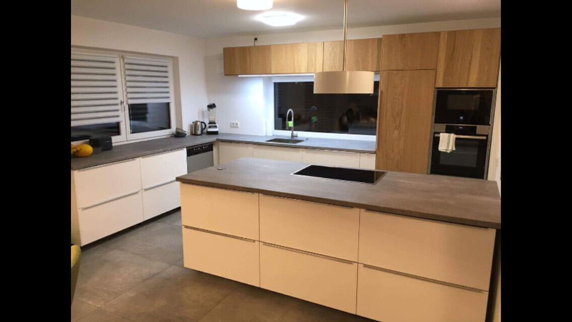 Modern kitchen with central island, white cabinets, and wood fronts, sink and oven.