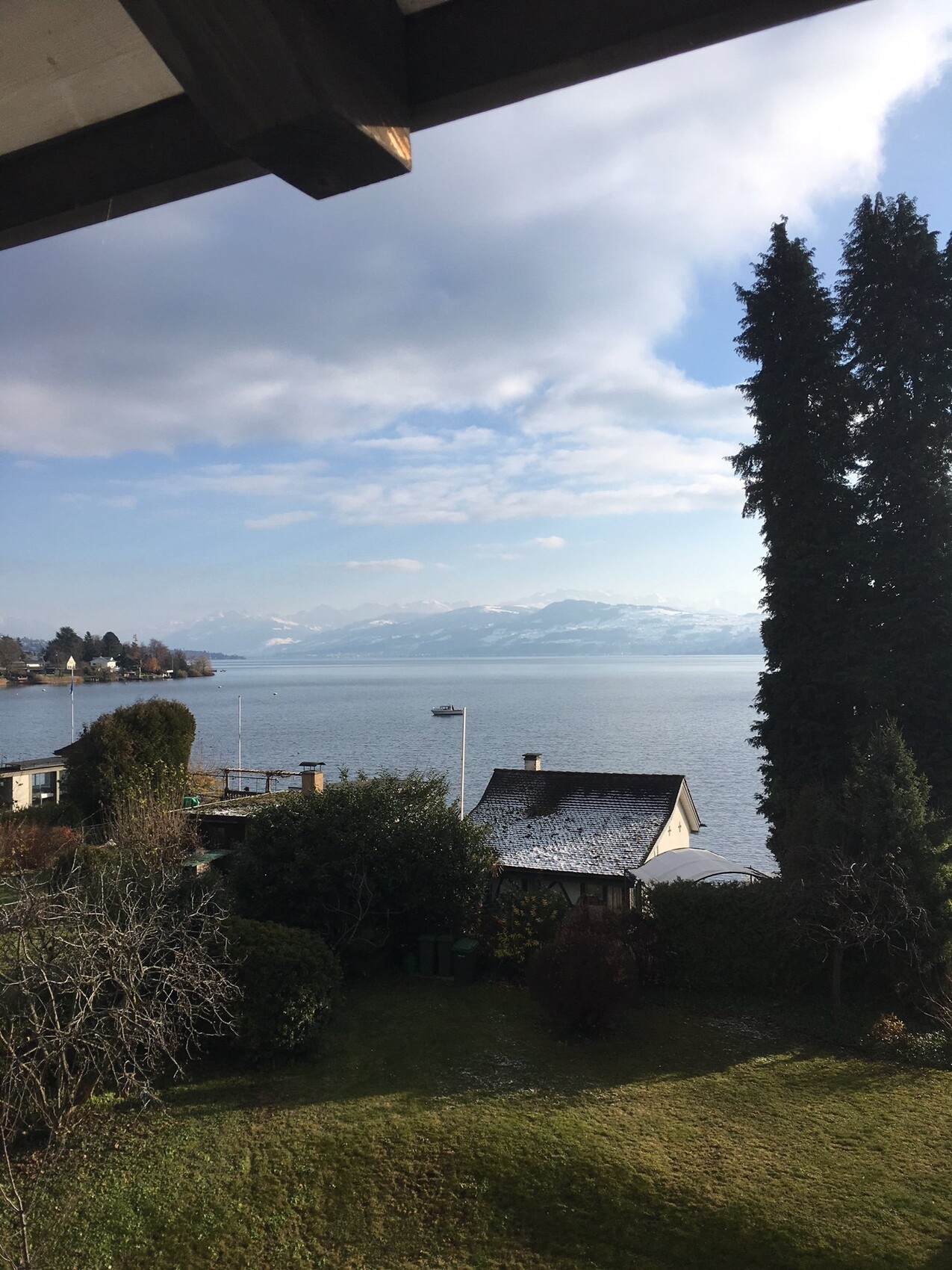 View from the balcony over the garden to the lake, houses on the shore, and mountain backdrop.