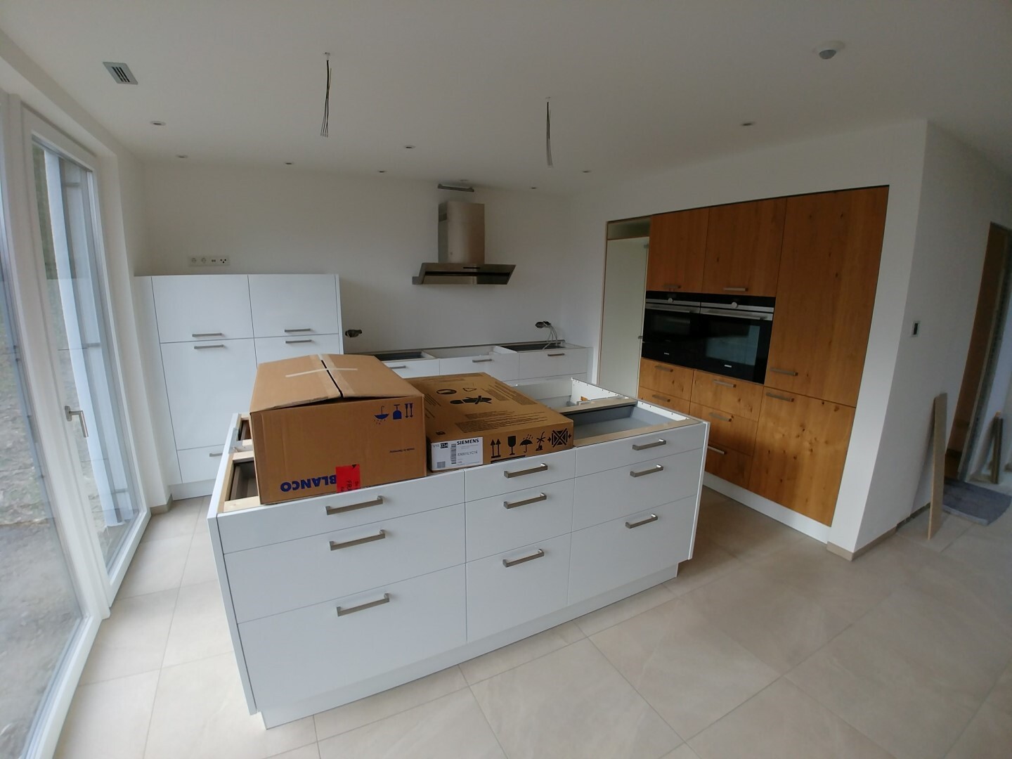 Modern kitchen with white island, wooden cabinets, and cardboard boxes; installation work.