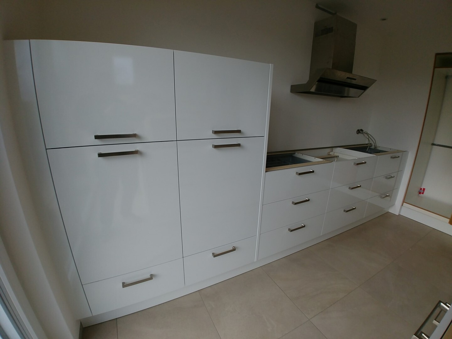 Modern white kitchen run with high-gloss fronts, extractor hood, and uninstalled cooktop