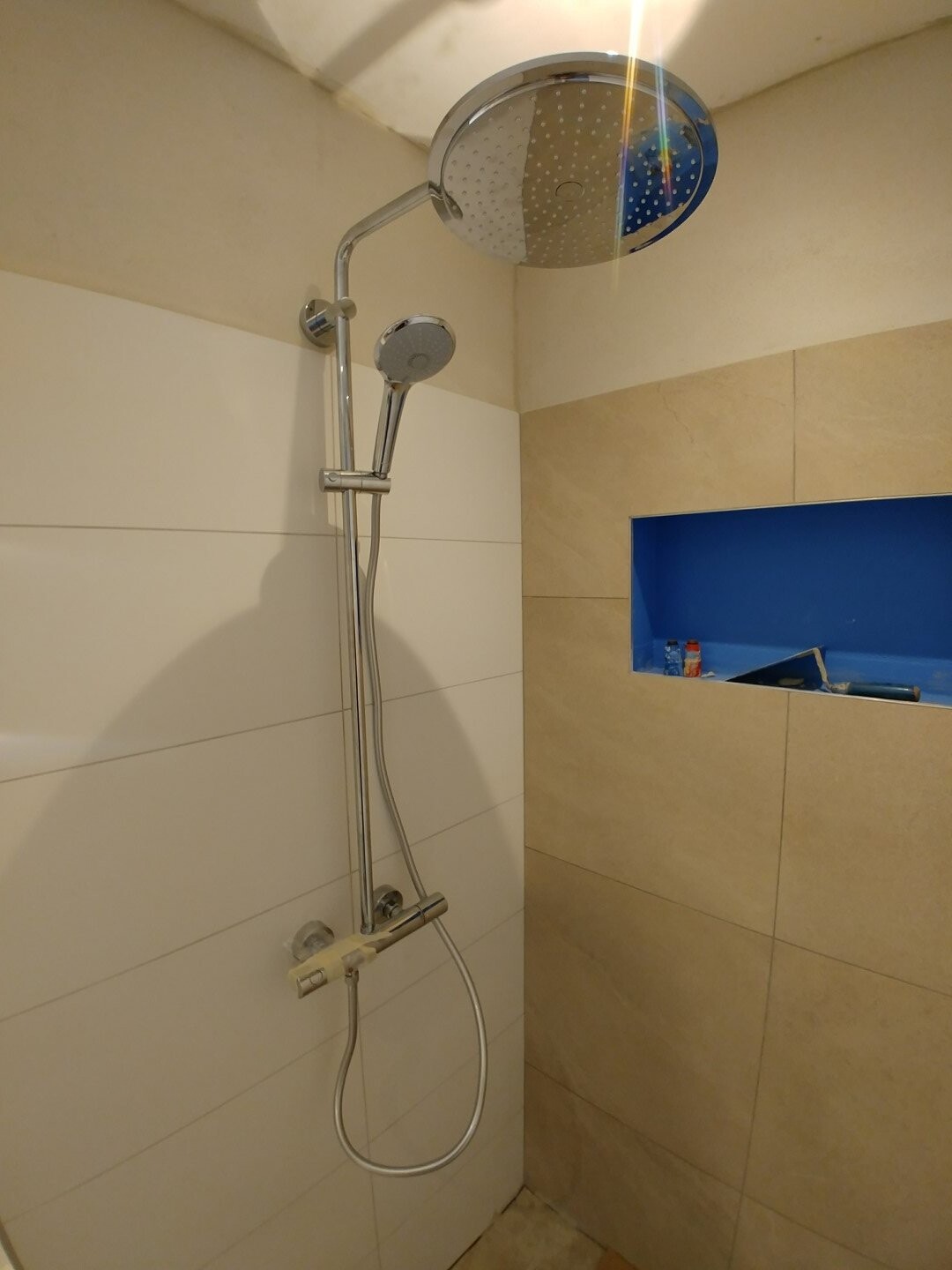 Large round rain shower head with hand shower, beige tiles, blue niche.