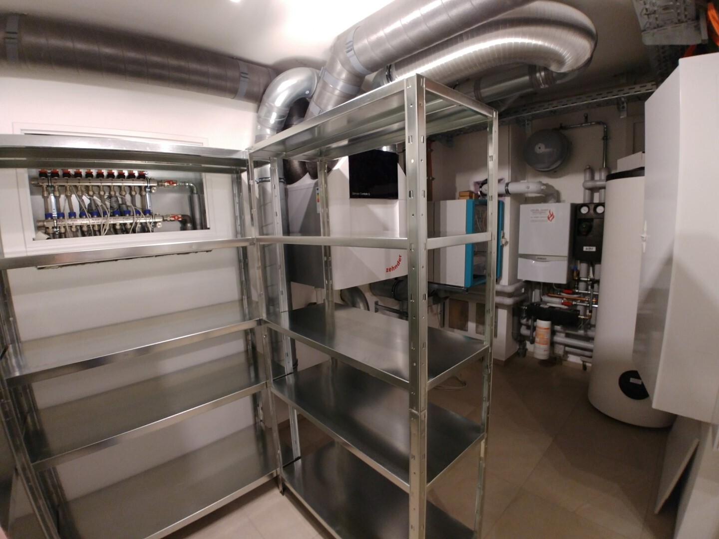 Utility room with metal shelves, piping, heating system, and ventilation ducts.